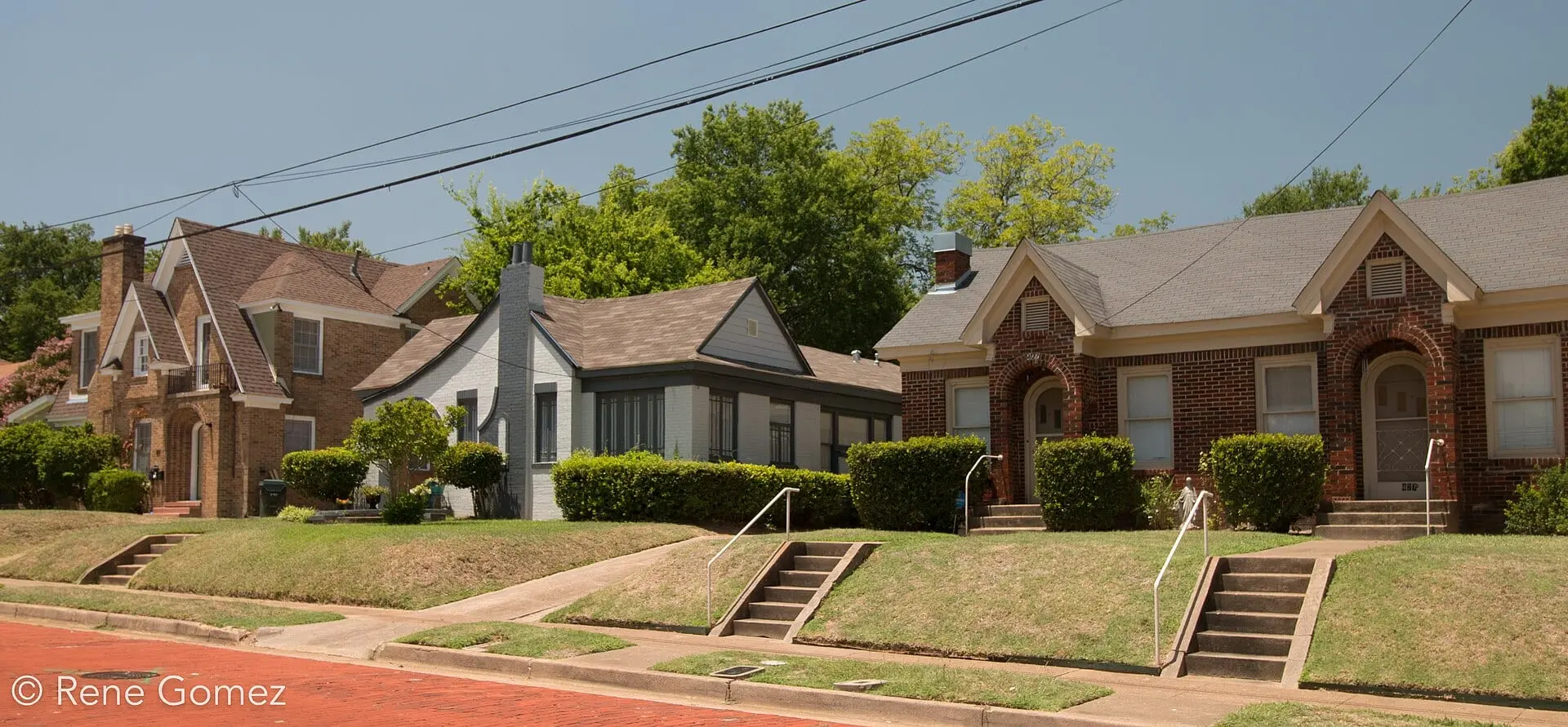 Brick and stucco cottages on a rise above a red-brick street, steps leading up from the curb.