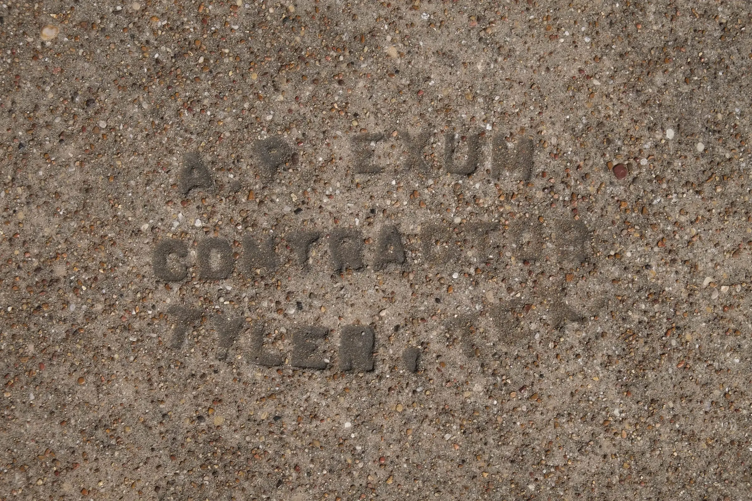 Letters pressed into a concrete sidewalk: “A. P. Exum, Contractor, Tyler, Tex.”