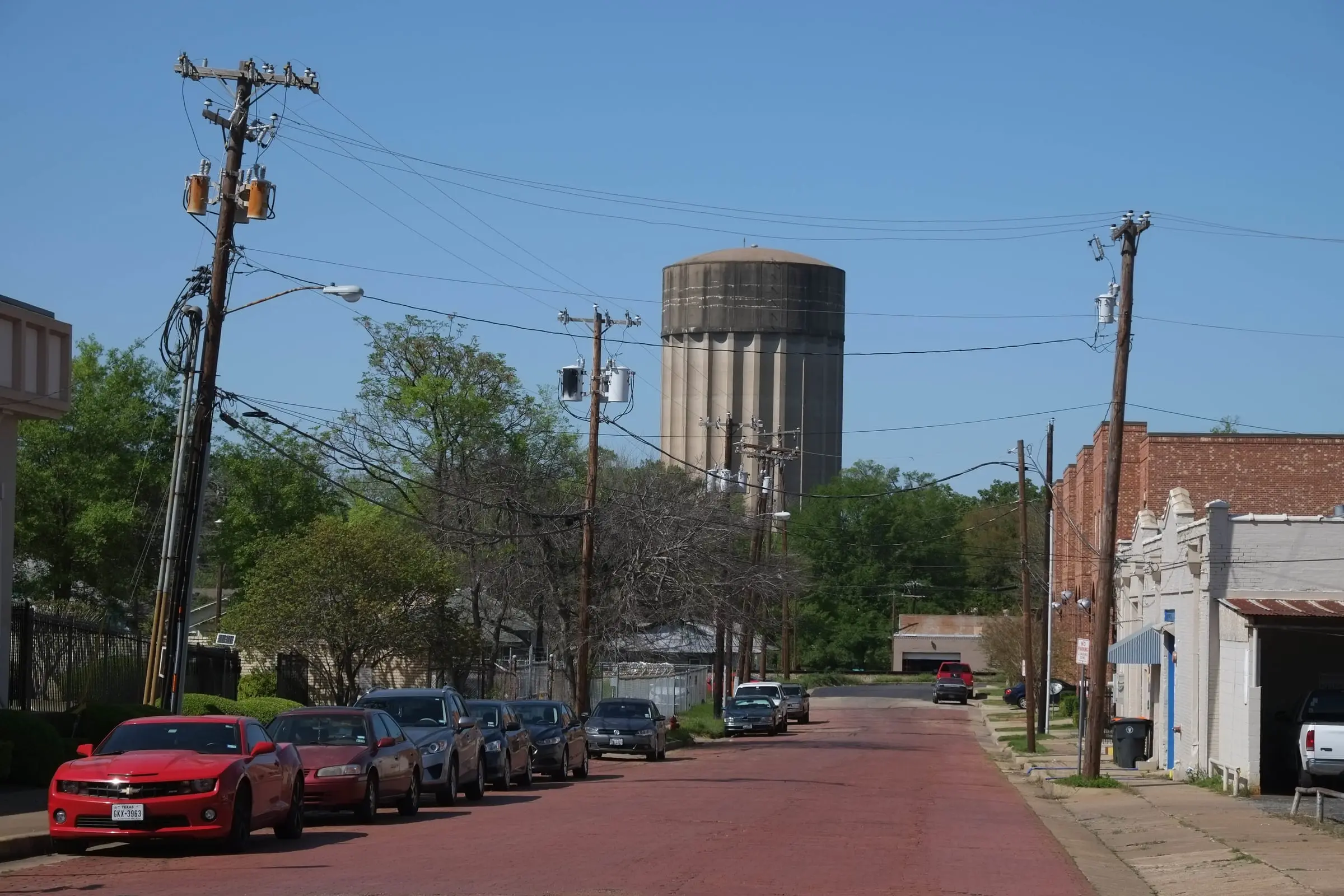 A brick-paved street running uphill between parked cars and utility poles, with a concrete water tower beyond.
