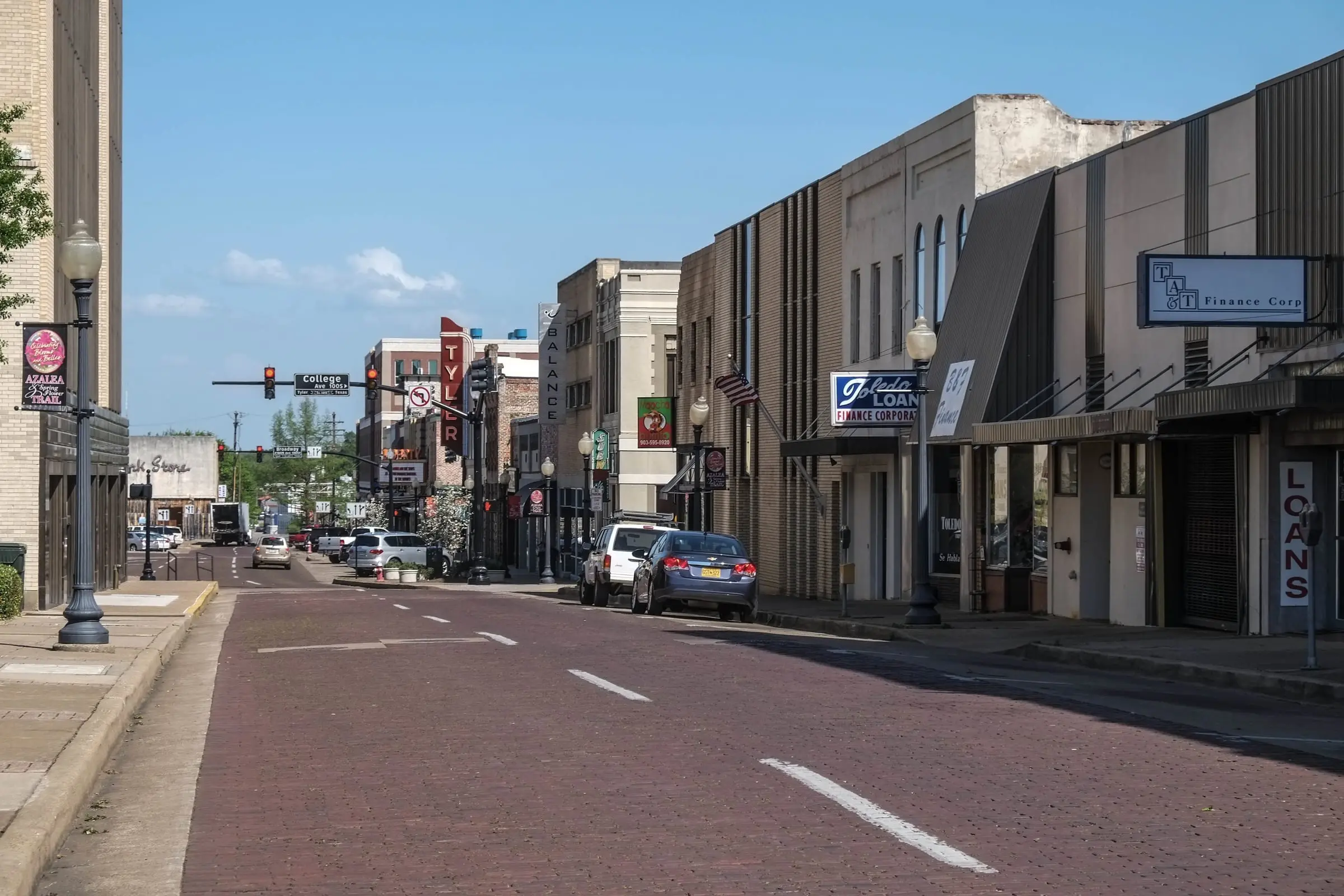 A long downtown avenue paved in dark red brick, with white lane lines, storefronts and a vertical sign reading TYLER in the distance.
