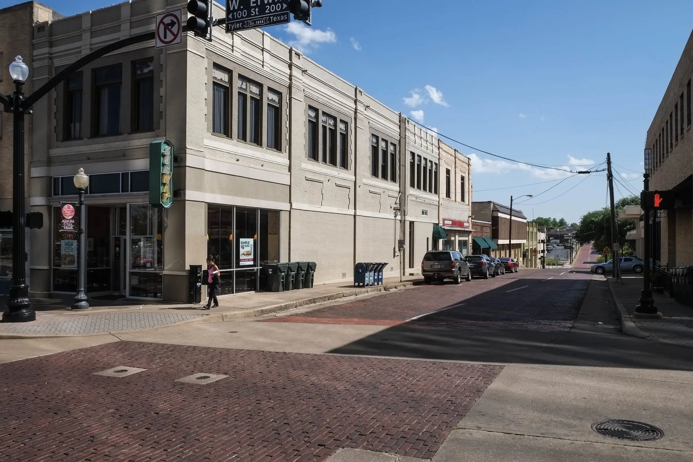 A downtown intersection paved in brick in front of a two-story commercial building, a street sign overhead.
