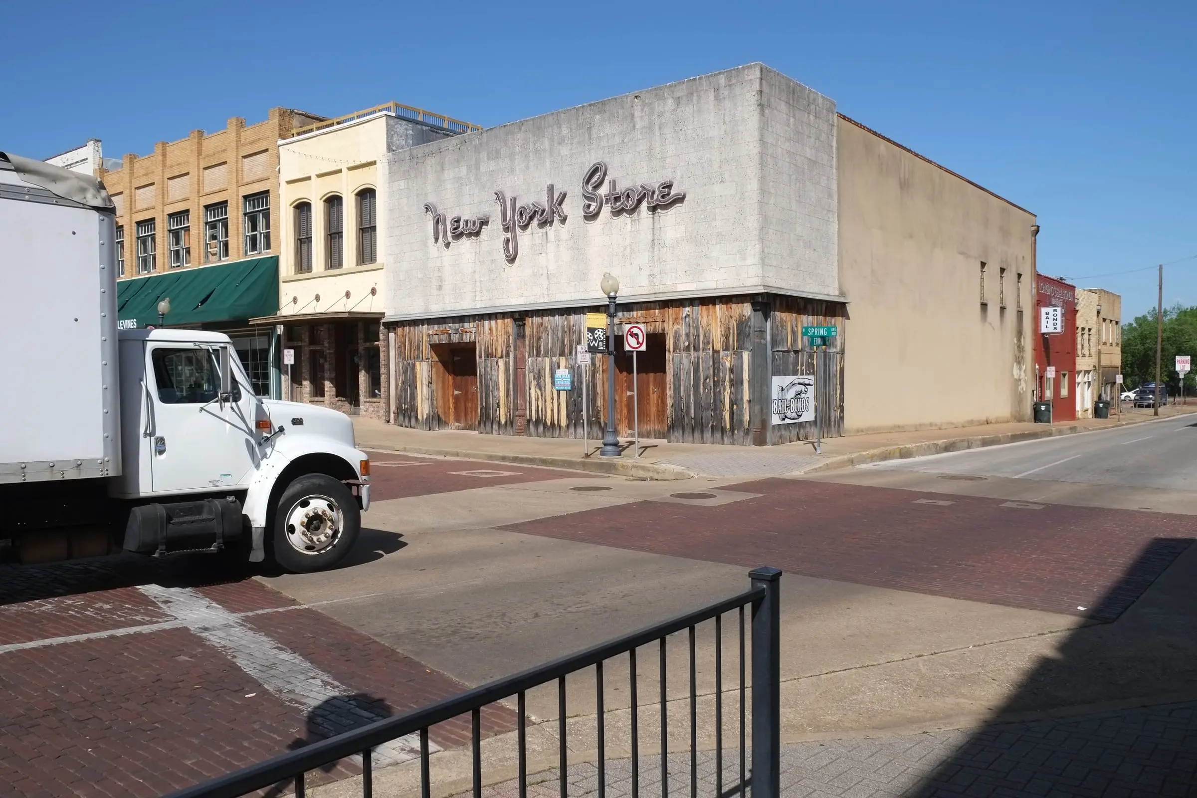 A brick-paved intersection in front of an old storefront lettered “New York Store,” a white truck at left.